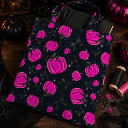 A fabric tote bag with a dark navy blue background and a repeating pattern of bright pink pumpkins and black spiders, styled on a dark wooden table with Halloween decorations.