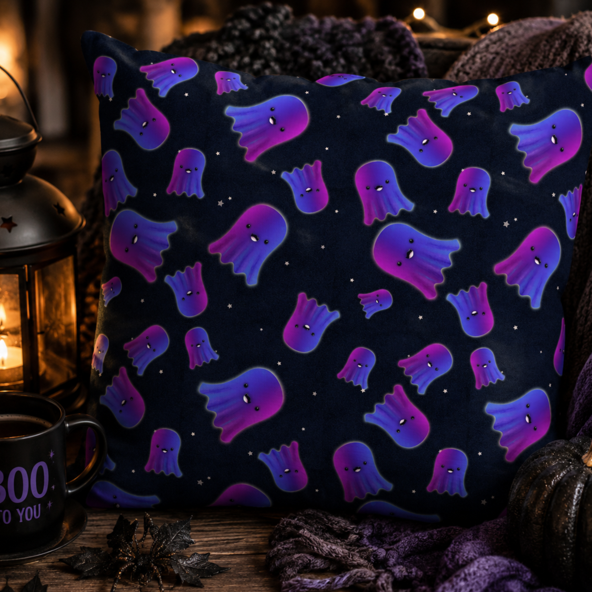 A square throw pillow with a dark navy blue background and a repeating pattern of purple and blue ghosts, styled in a cozy autumn setting with a lantern, mug, and knit blankets.